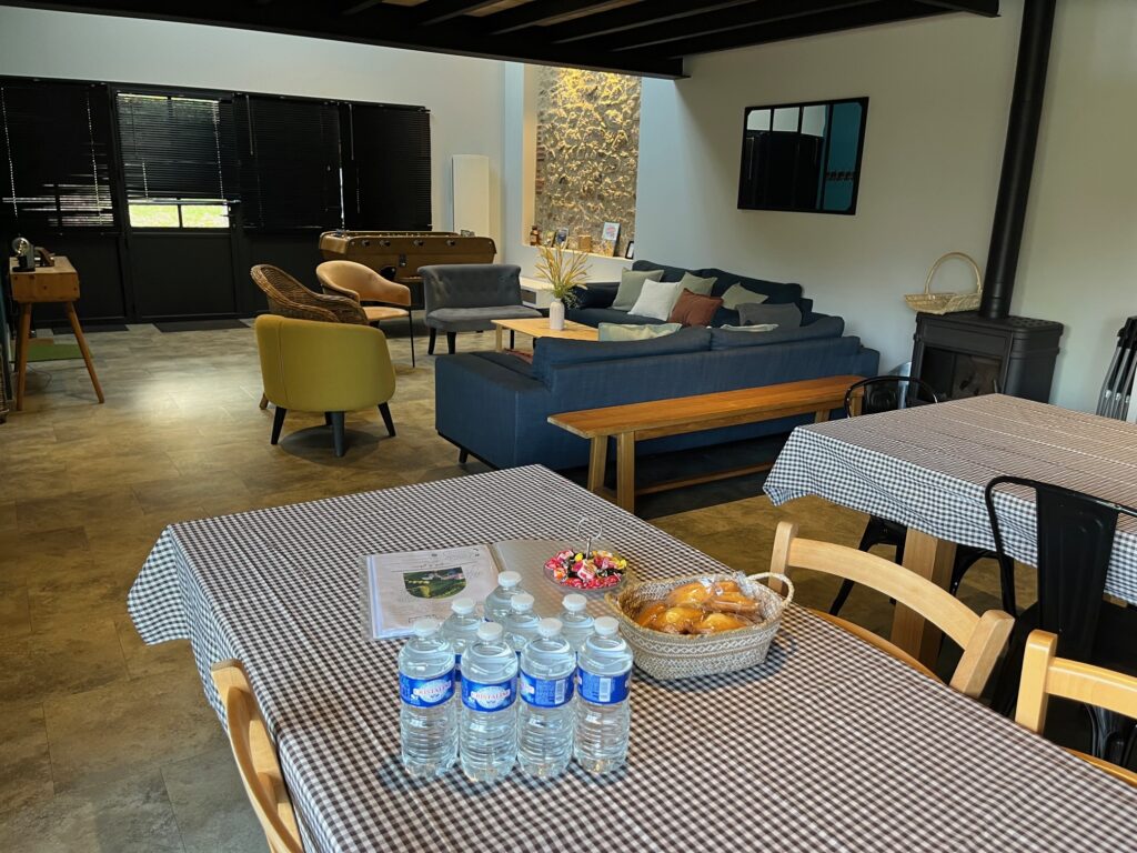 Une salle avec des tables recouvertes de nappes à carreaux, des bouteilles d'eau, des pâtisseries, un bol de bonbons, des sièges de salon et un baby-foot à l'arrière-plan.