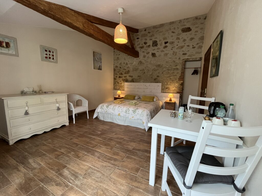 Une chambre confortable avec un lit double blanc, des tables de chevet avec lampes, une commode blanche, une table avec deux chaises et un mur d'accent en pierre.