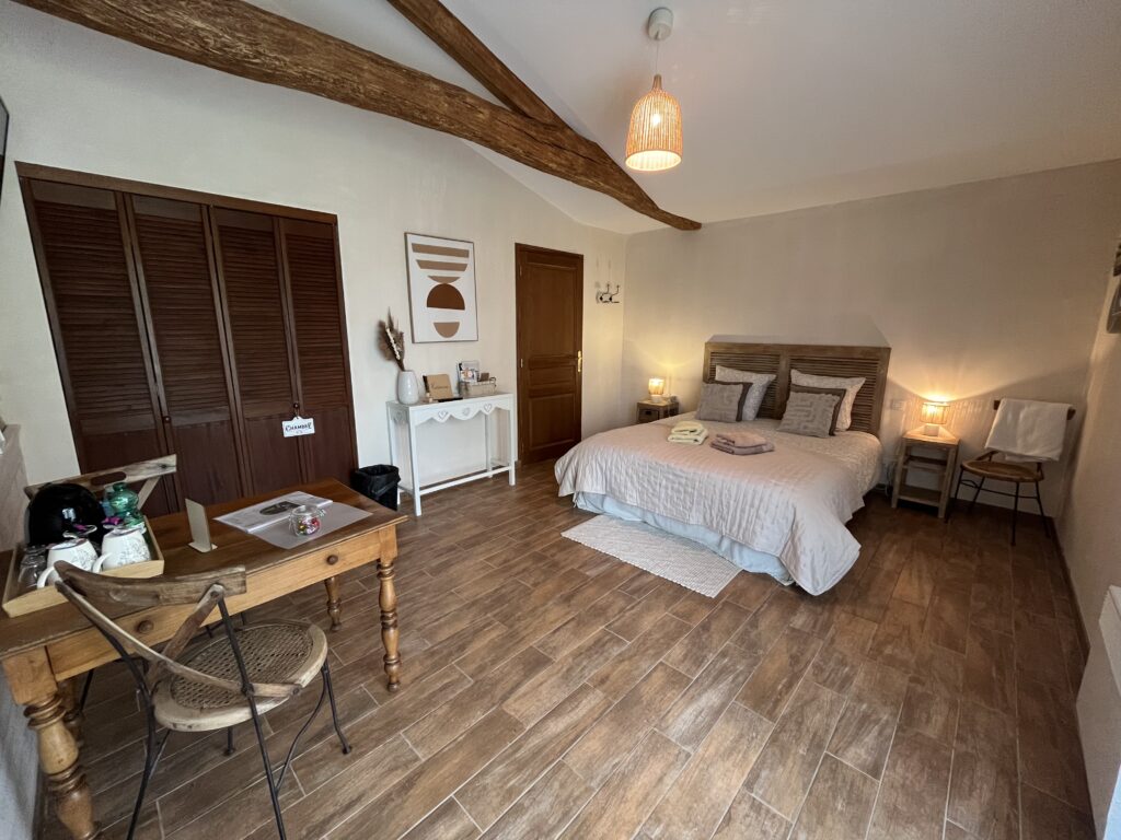 Une chambre confortable avec un lit double, un plancher en bois, un petit bureau, une chaise, une armoire, des tables de chevet avec des lampes et des poutres rustiques au plafond.